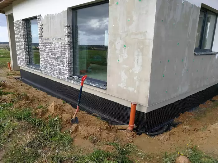 Basement waterproofing being installed around the edges of a foundation