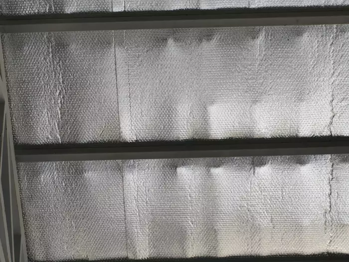 A detailed view of a reflective insulation material, possibly foil-backed, installed between dark horizontal beams, creating a textured and crinkled silvery surface.